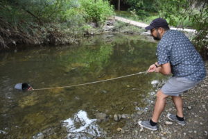 Volunteer collects water sample from stream with a bucket tied to a rope.