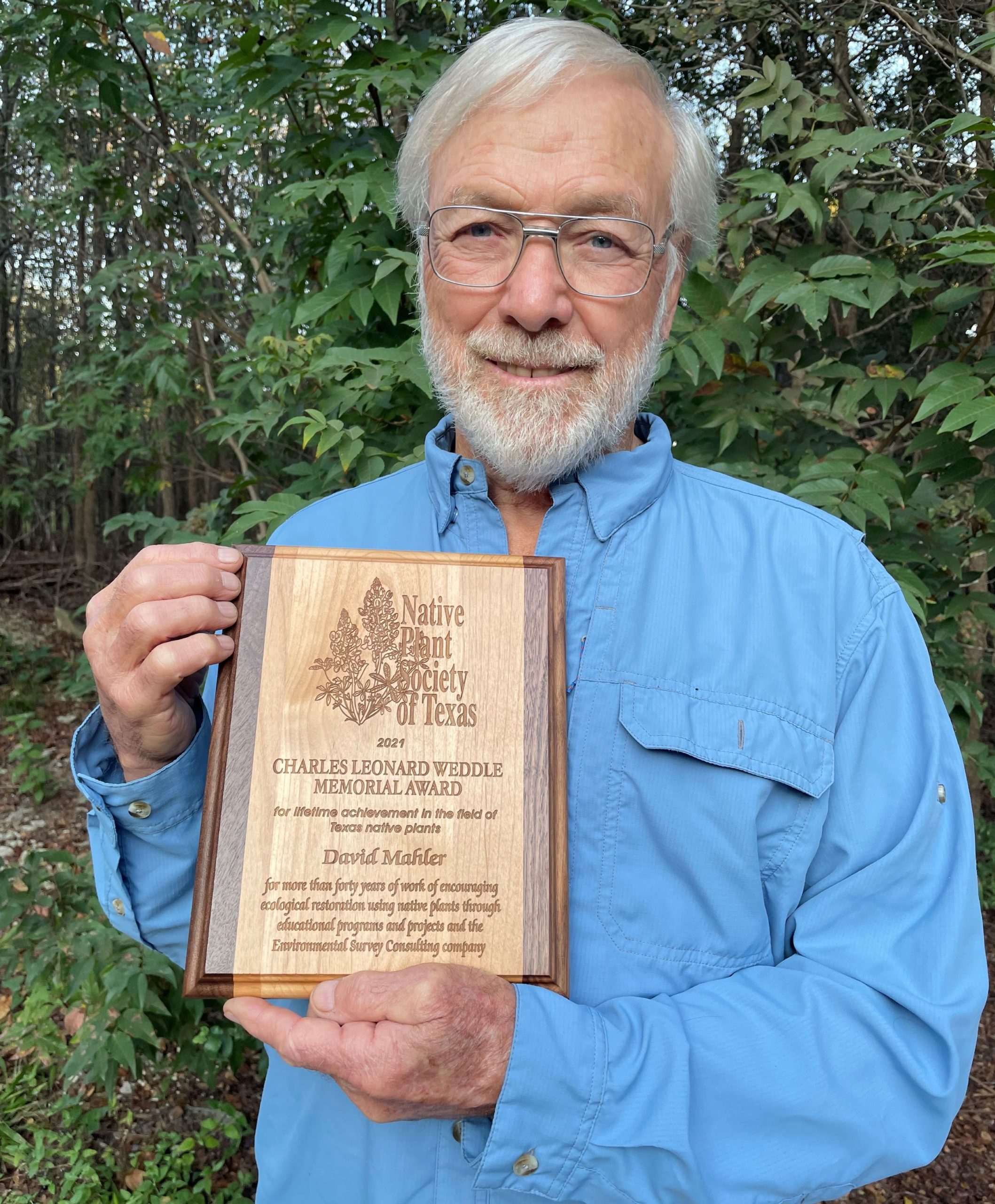 David Mahler standing with NPSOT award in front of native trees and plants